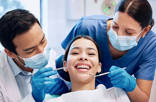 Dentist and dental assistant looking at smiling patient's teeth