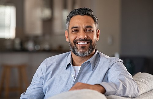 Man with blue shirt smiling on couch at home